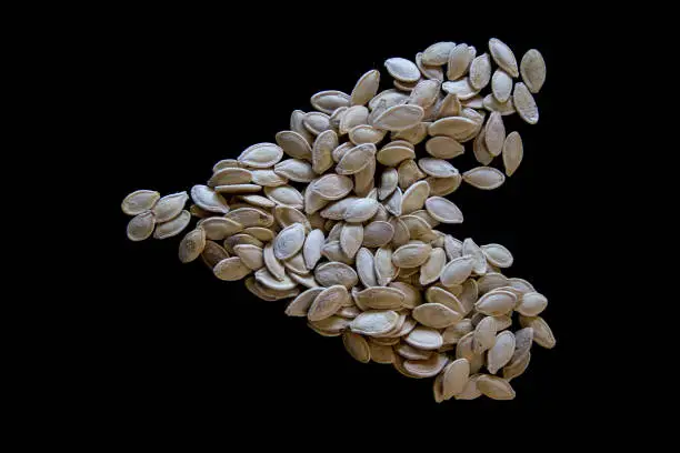 Roasted salty pumpkin seeds in the shape of a heart, black background