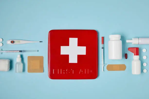 Photo of top view of red first aid kit box on blue surface with medical supplies