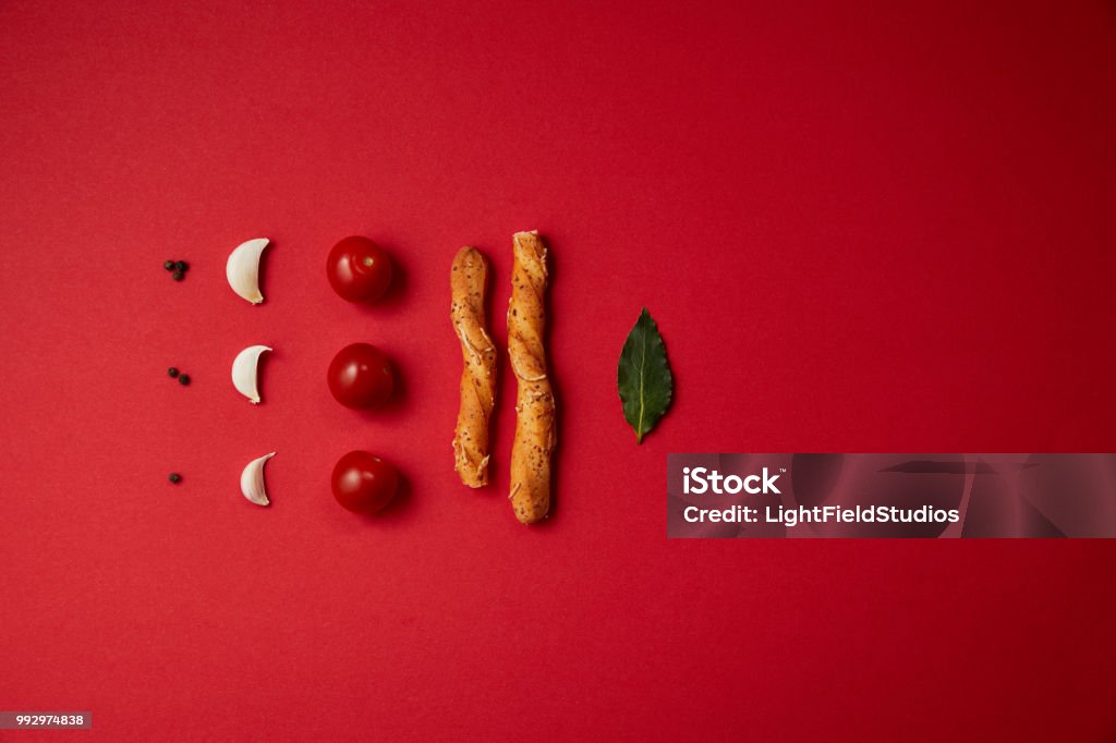 food styling of tasty tomatoes, garlic, bread sticks and bay leaf on red table Food Stock Photo