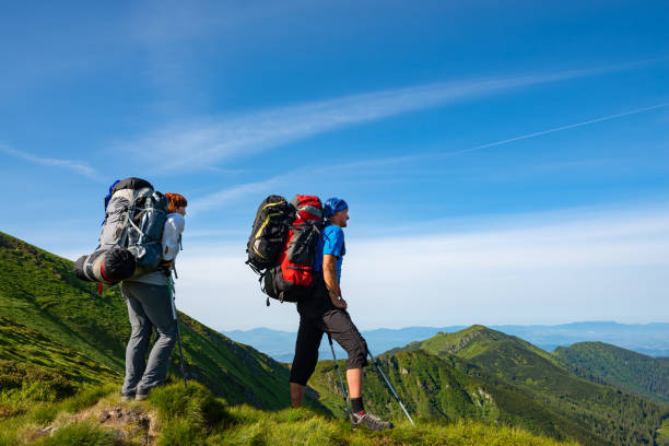 Adventurers with backpacks stands on green mountain ridge