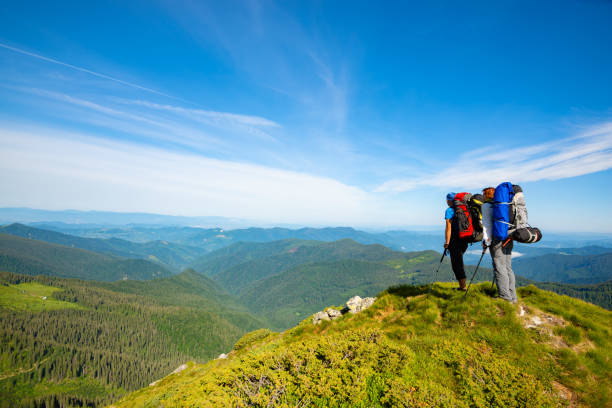 Adventurers with backpacks stands on green mountain ridge
