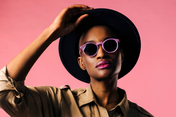 A fashion portrait of a young woman with purple sunglasses and black hat A fashion portrait of a young woman with purple sunglasses and black hat, isolated on pink studio background young cool girl stock pictures, royalty-free photos & images