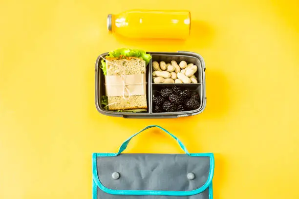 Lunchbox with food - a sandwich, nuts and berries - next to a bottle of orange juice and a bag for a luncheon. Food you can take with you. Top view, flat lay,