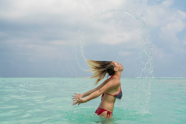美しい若い女性は海でお楽しみいただけます。 - splashing maldives human hair spray ストックフォトと画像