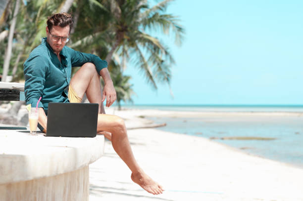 man freelancer with laptop sitting at the beach - on beach laptop working imagens e fotografias de stock