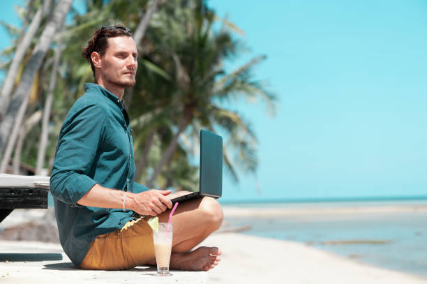istock Man freelancer with laptop sitting at the beach 993090776