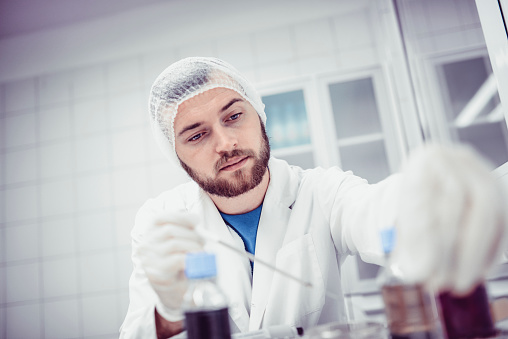 Scientist Reaching For Bottle Containing Ingredient Needed To Make Compound