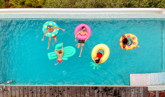 Aerial view of group of friends having fun on inflatable rings in the pool