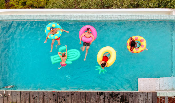 amigos se divertindo em anéis infláveis na piscina - floating on water swimming pool men water - fotografias e filmes do acervo