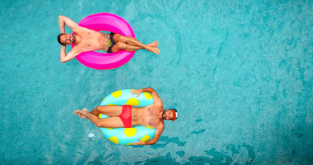 Two man relaxing on inflatable rings Aerial view of a two men relaxing on a inflatable rings and floating in the pool man gay stock pictures, royalty-free photos & images