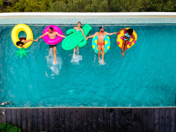 amigos se divertindo em anéis infláveis na piscina - floating on water swimming pool men water - fotografias e filmes do acervo