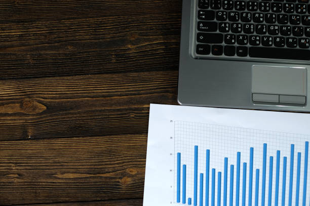 istock Notebook laptop computer and financial graph on white paper on working table, business planning vision and finance analysis concept. 993197908