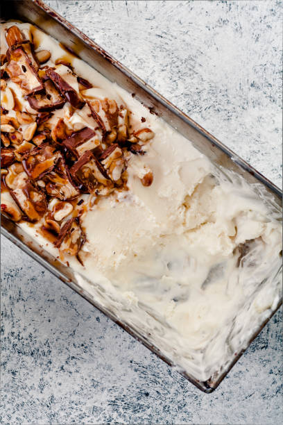 istock Caramel ice cream half way scooped from metallic container. Peanuts and chocolate used for decoration. Top view with copy space. Rustic textured background. 993235834