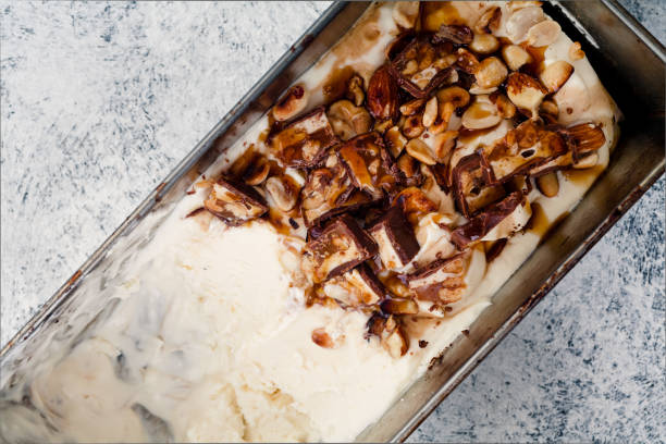 istock Caramel ice cream half way scooped from metallic container. Peanuts and chocolate used for decoration. Top view with copy space. Rustic textured background. 993235848