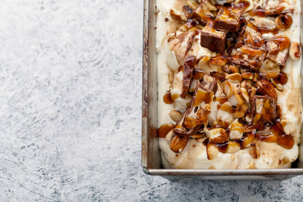 istock Snickers ice cream with caramel,  fried peanuts and hazelnuts in metallic baking tray on rustic background. Gourmet summer treat concept. Composition with copy space. 993238020