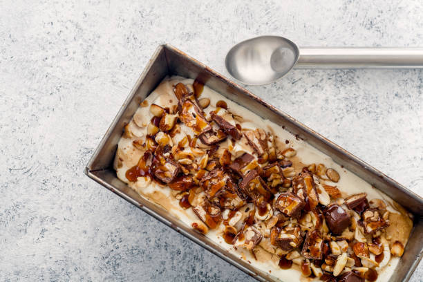istock Snickers ice cream with caramel,  fried peanuts and hazelnuts in metallic baking tray on rustic background. Gourmet summer treat concept. Composition with copy space. 993238130