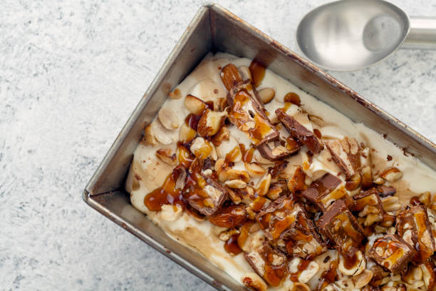 istock Snickers ice cream with caramel,  fried peanuts and hazelnuts in metallic baking tray on rustic background. Gourmet summer treat concept. Composition with copy space. 993238138