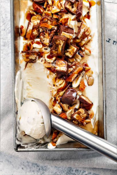 istock Snickers ice cream with caramel,  fried peanuts and hazelnuts in metallic baking tray on rustic background. Scoop with a ball. Gourmet summer treat concept. Composition with copy space. 993240262
