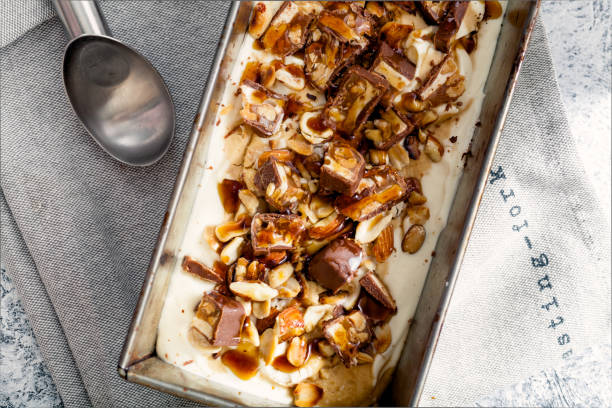 istock Snickers ice cream with caramel,  fried peanuts and hazelnuts in metallic baking tray on rustic background. Gourmet summer treat concept. Composition with copy space. 993240282
