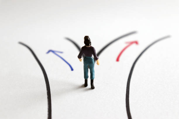 a miniature woman standing in front of two different path. - turning point imagens e fotografias de stock