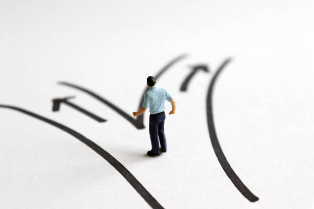 a miniature man standing in front of two different path. - turning point imagens e fotografias de stock