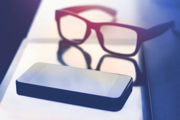 istock smartphone tablet and eyeglasses laying on table, dark tone 993342128