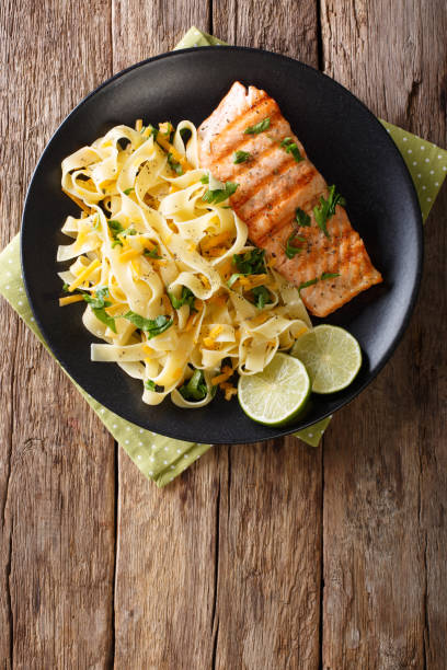 istock Pasta fetuccini with cheddar cheese and grilled salmon on a plate close-up. vertical top view 993347054