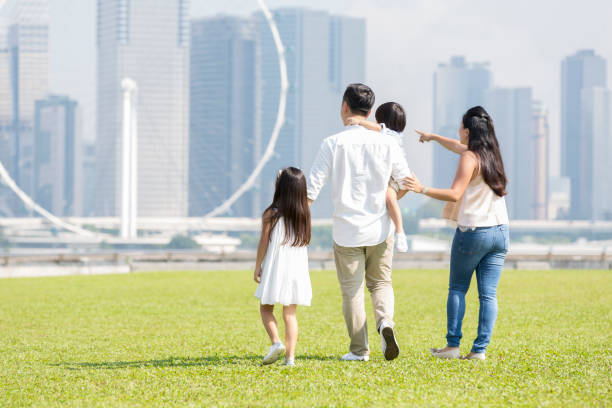 Rear view of family walking together Mom and dad with their two children walk together in a city park. A city skyline and ferris wheel are in the background. happy malay couple stock pictures, royalty-free photos & images