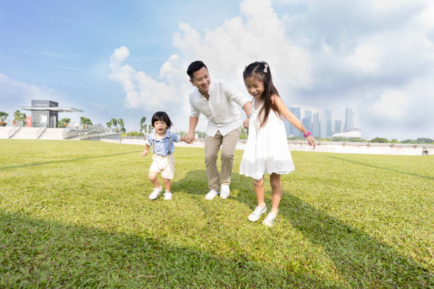 Mid adult dad walks with his son and daughter in a city park.