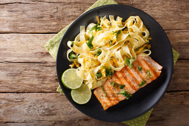 pasta fetuccini con queso cheddar y salmón a la parrilla en un primer plano de la placa. vista superior horizontal - food dinner prepared fish gourmet fotografías e imágenes de stock