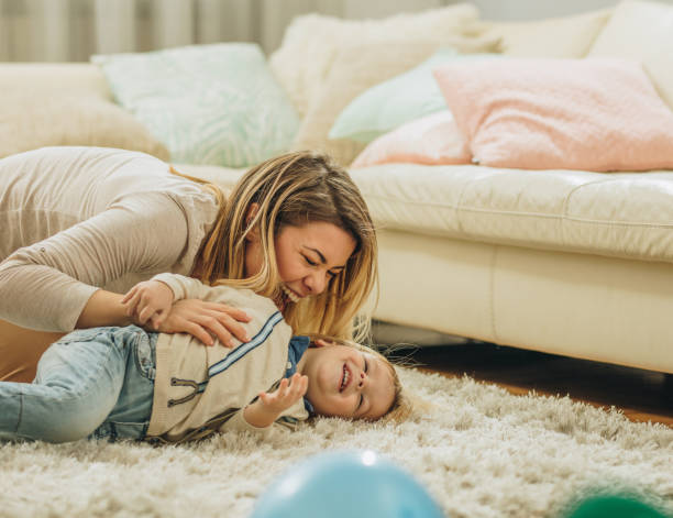 istock Young cheerful mother having fun while playing with her small boy on carpet at home. 993389358
