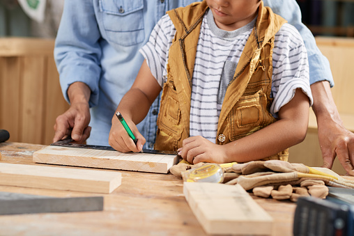 Cropped image of boy marking wooden plank under control of his father