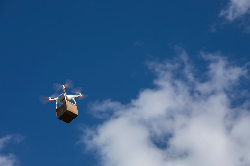 DJI Phantom 4 drone delivering a cardboard box on a blue sky.