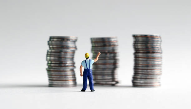 un uomo in miniatura che cerca una pila di tre monete. - minimum wage foto e immagini stock