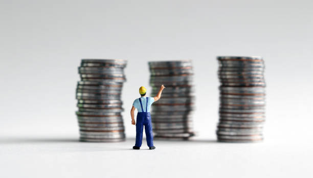 A miniature man reaching for a pile of three coins. stock photo