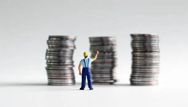 Photo of A miniature man reaching for a pile of three coins.