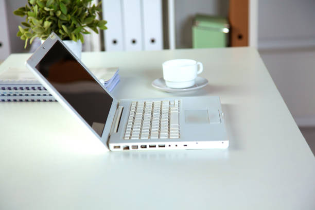 istock Close up view of a work desk interior with a laptop computer, a cup of coffee and white curtains on a sunny day 993419150