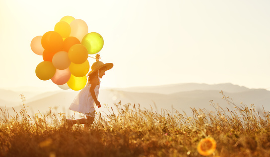 young happy child girl with balloons at sunset in summer