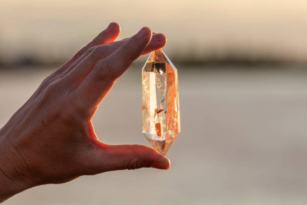 une main tenant un cristal de quartz bel à l’extérieur au soleil - transparent crystal crystal ball human hand photos et images de collection