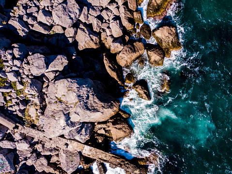 aerial overhead view of waves crash into the stone rocky sea coast