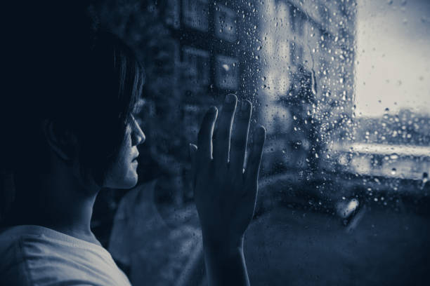 istock sadly woman looking out at windows raining drops dark mood dim light 993463916