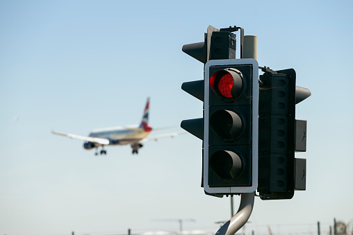 Heathrow, UK - June 27, 2018: Landing British Airways airplane at Heathrow airport, seen behind a street red light.