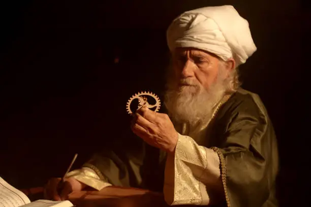 An old and historic Islamic scientist is working in his studio writing, reading and exploring.