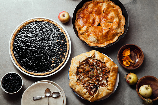 Variety of autumn pies: blueberry tart, chantarelle galette and classical apple pie with sweet pastry crust. Harvest time baking concept. Concrete rustic background.