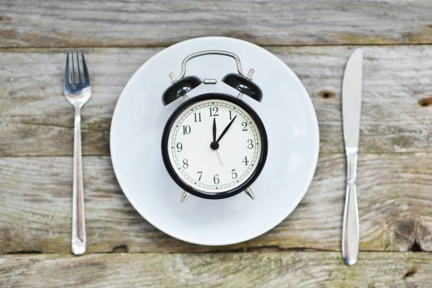 istock Time to eat with clock plate fork and knife on a table 993524634