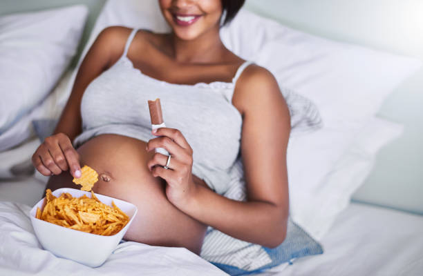 Blame it on the pregnancy! Cropped shot of a pregnant woman enjoying a chocolate and potato chips in bed family eating potato chips stock pictures, royalty-free photos & images