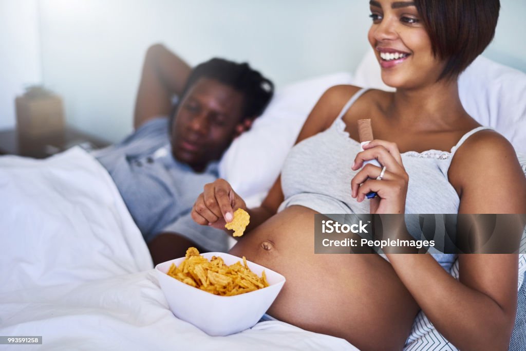 Settling my cravings with some happy snacks Cropped shot of a pregnant woman enjoying a chocolate and potato chips in bed Pregnant Stock Photo