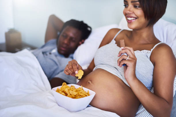 Settling my cravings with some happy snacks Cropped shot of a pregnant woman enjoying a chocolate and potato chips in bed family eating potato chips stock pictures, royalty-free photos & images