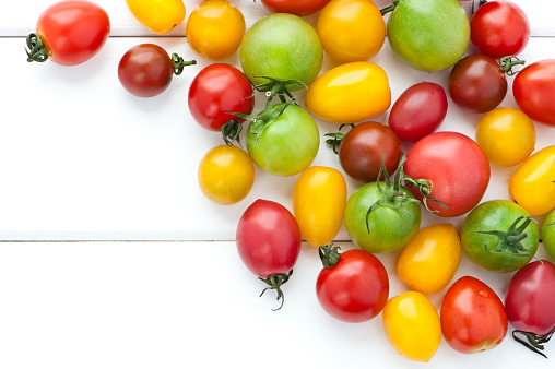 wet multi colored cherry tomatoes on white wooden background
