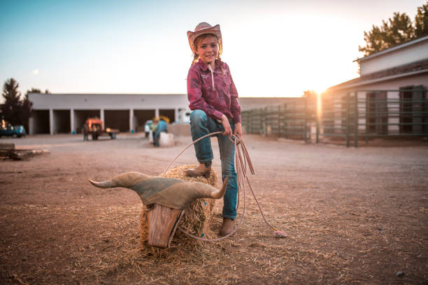 Young cowgirl is training how to lassoing on a ranch in rodeo arena in Utah, USA. She is throwing lasso.
